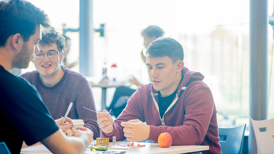 A student speaking to two other students who are undertaking a building activity